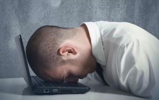 Photo of frustrated man with head on laptop