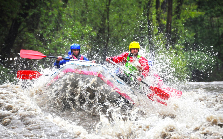 two men riding a wave while white-water rafting